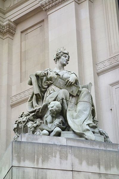 Stone sculpture of woman with child reading in front of important building