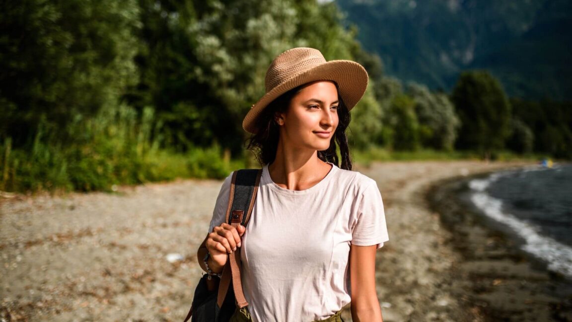 woman wearing a hat near a river with the forest in the background.