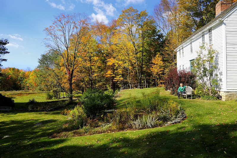 Human relaxes outside of old house at Hancock Shaker Village amount fall leaves