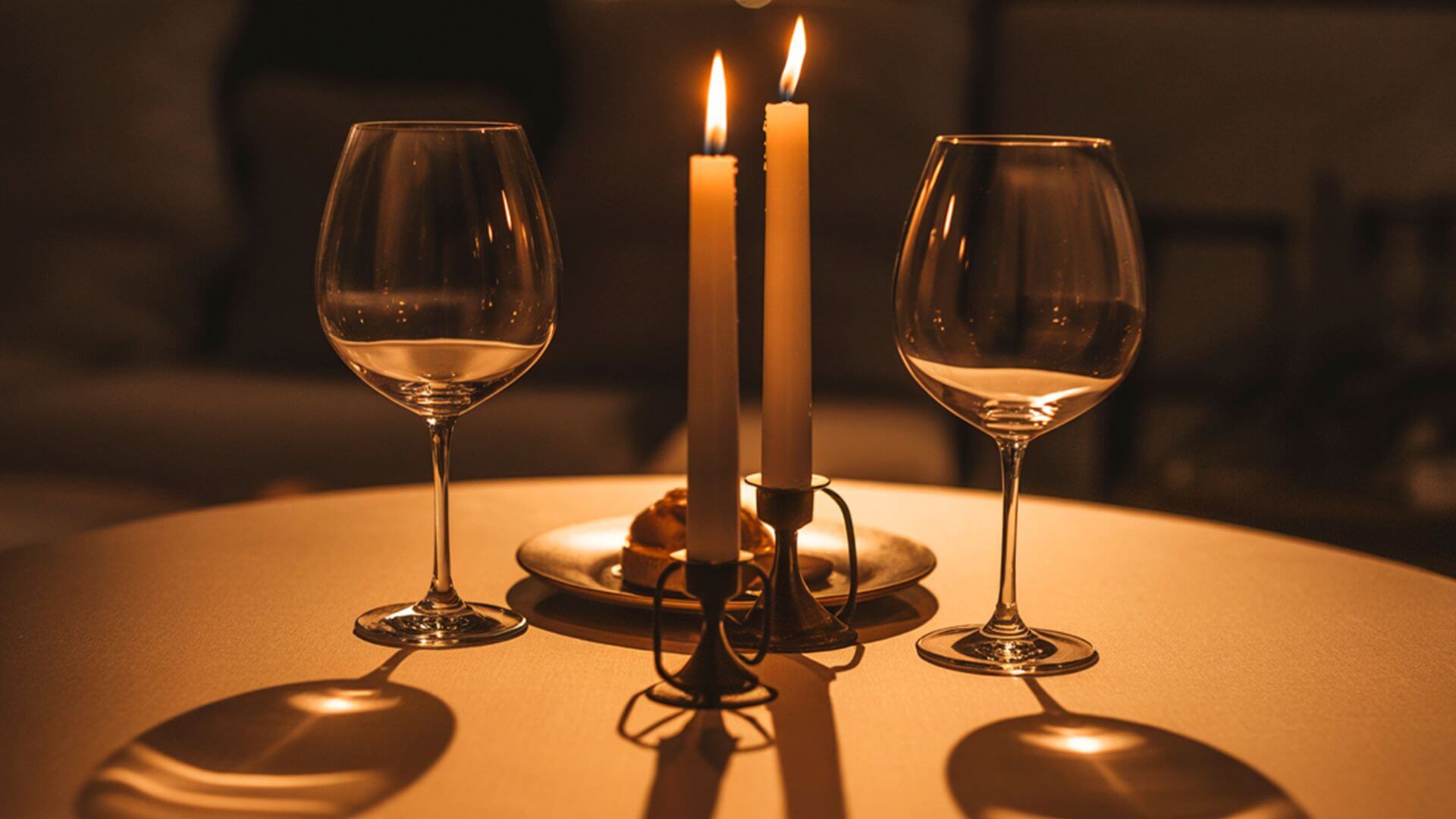 candle lit table with two wine glasses and burning candles creating a romantic dinner setting