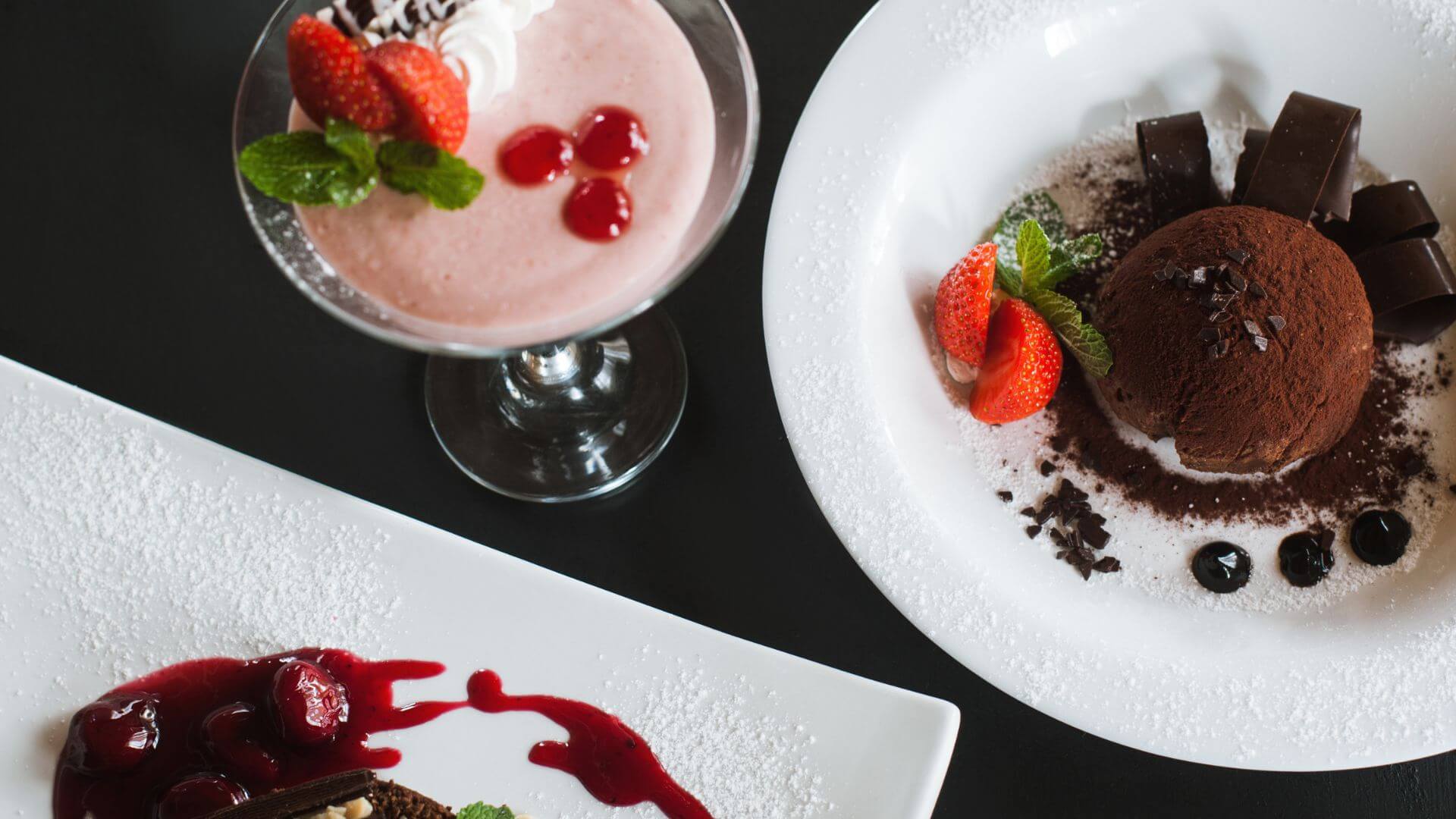 plated desserts including chocolate cake strawberry mousse and garnishes on a dark table