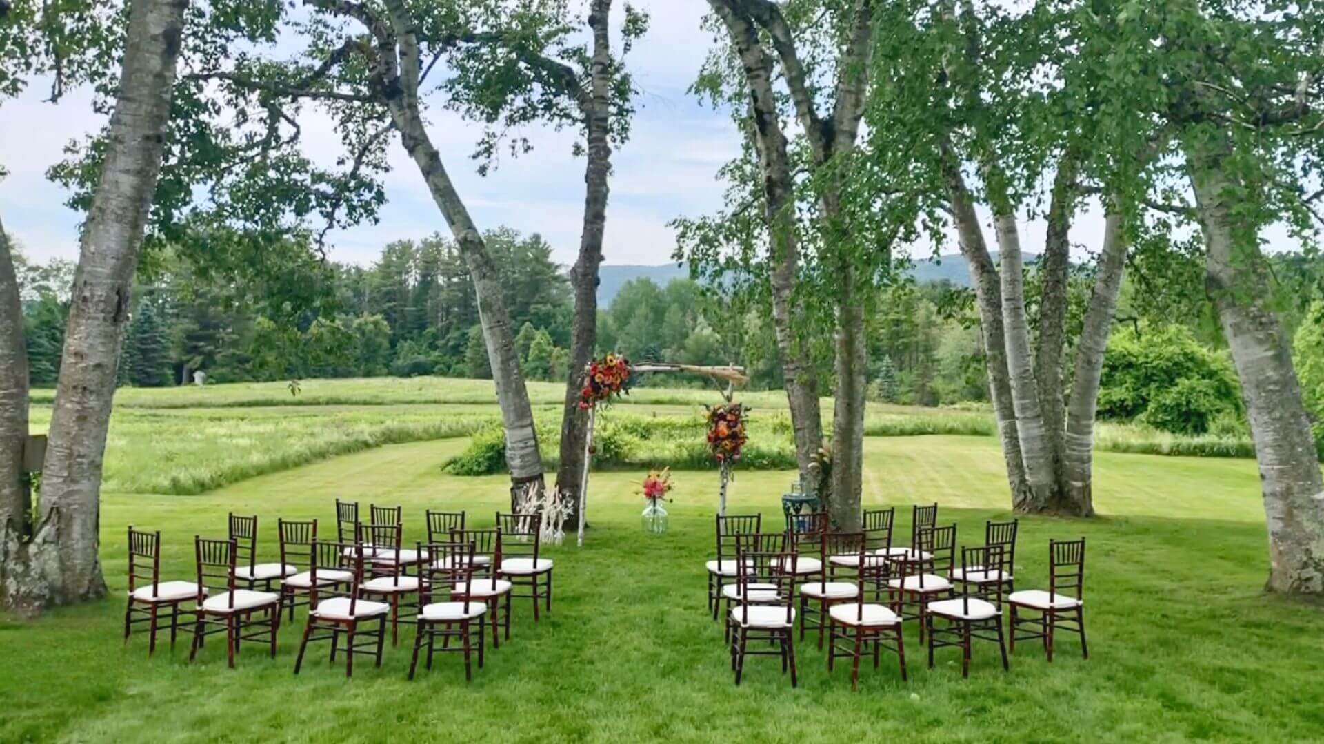 rows of chairs set up on a lawn for an outdoor berkshires wedding venue at devonfield inn beneath tall trees