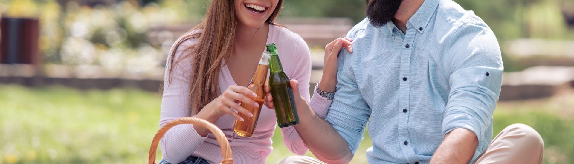 A couple drinks beer while having a picnic on a blanket outside in a park