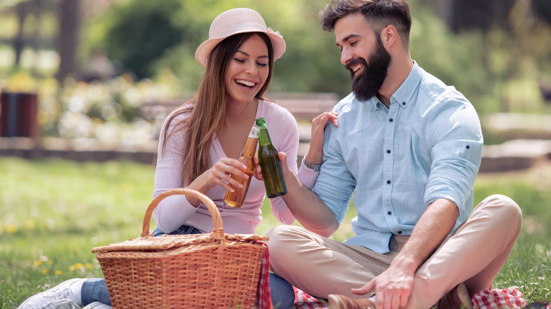 A couple drinks beer while having a picnic on a blanket outside in a park