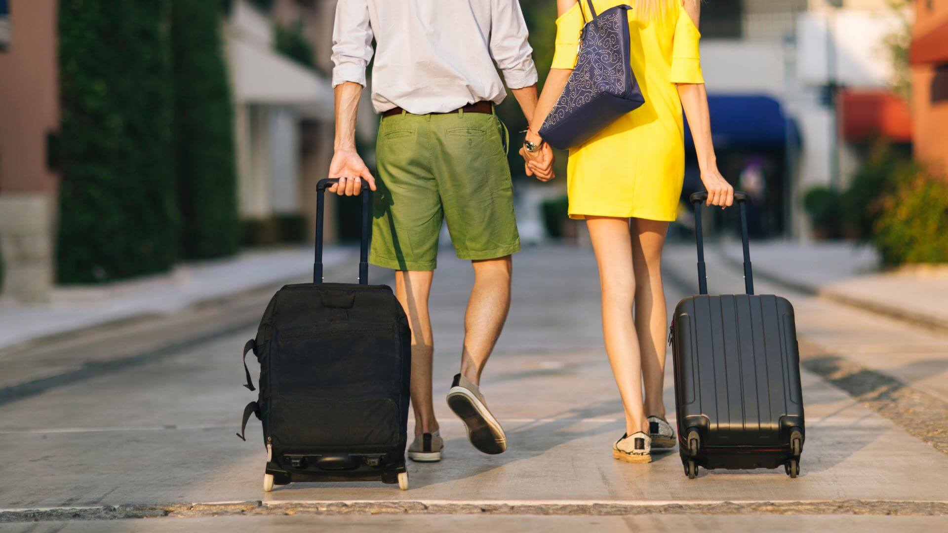 A couple holding hands walking down the street rolling their luggage behind them