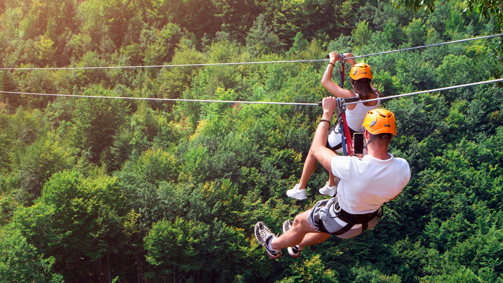 Two people zip lining over a forested area.