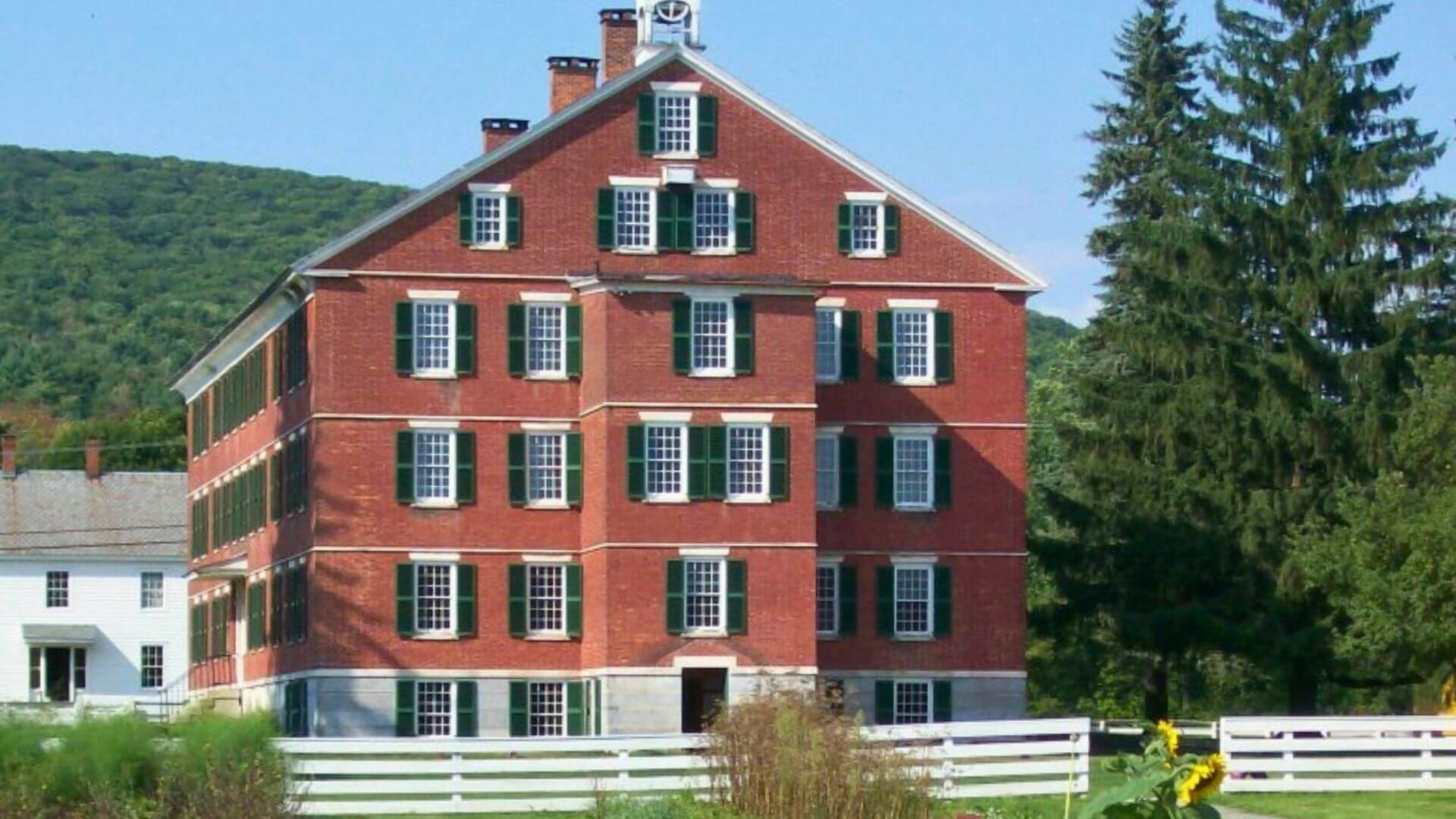 A red brick dwelling building with green shutters at Hancock Shaker Village in Pittsfield, MA.