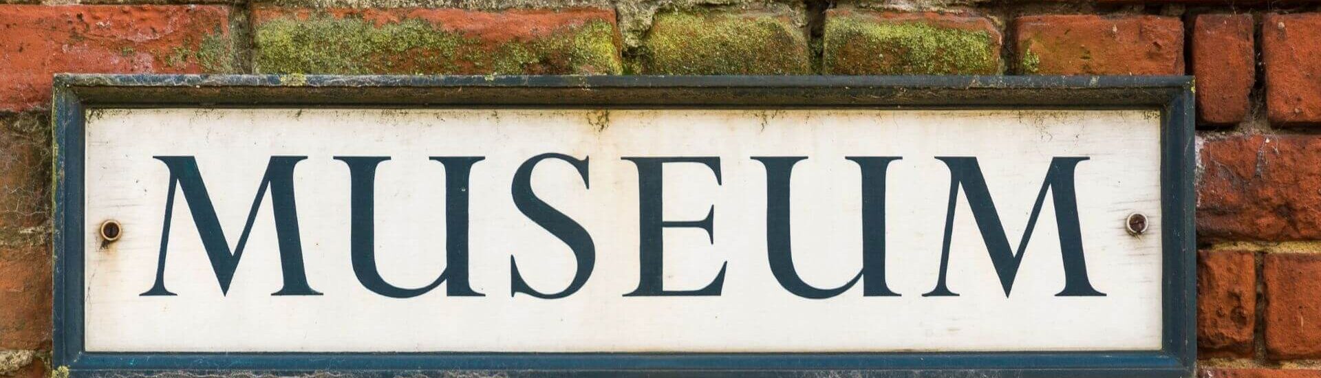 A weathered museum sign mounted on a brick wall.