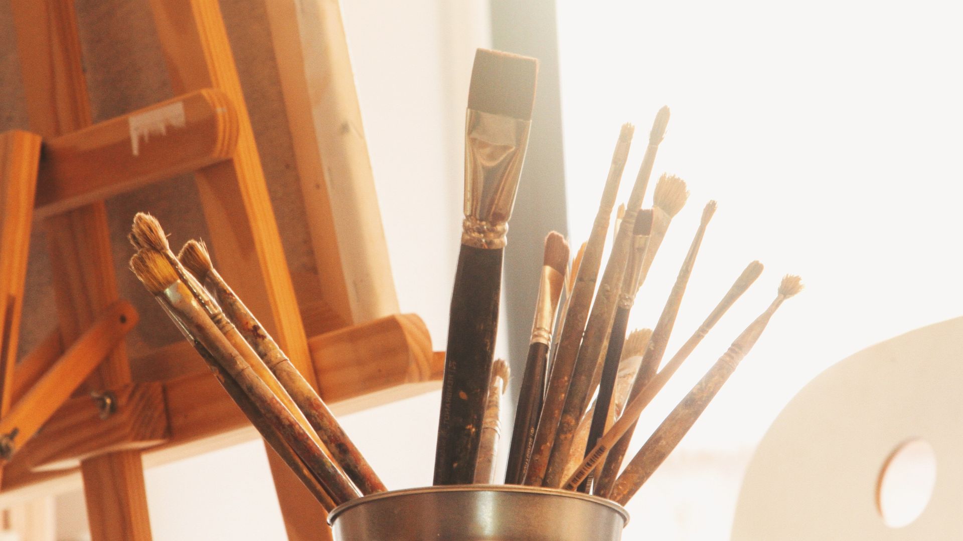 An easel, can of paint brushes, and palette.