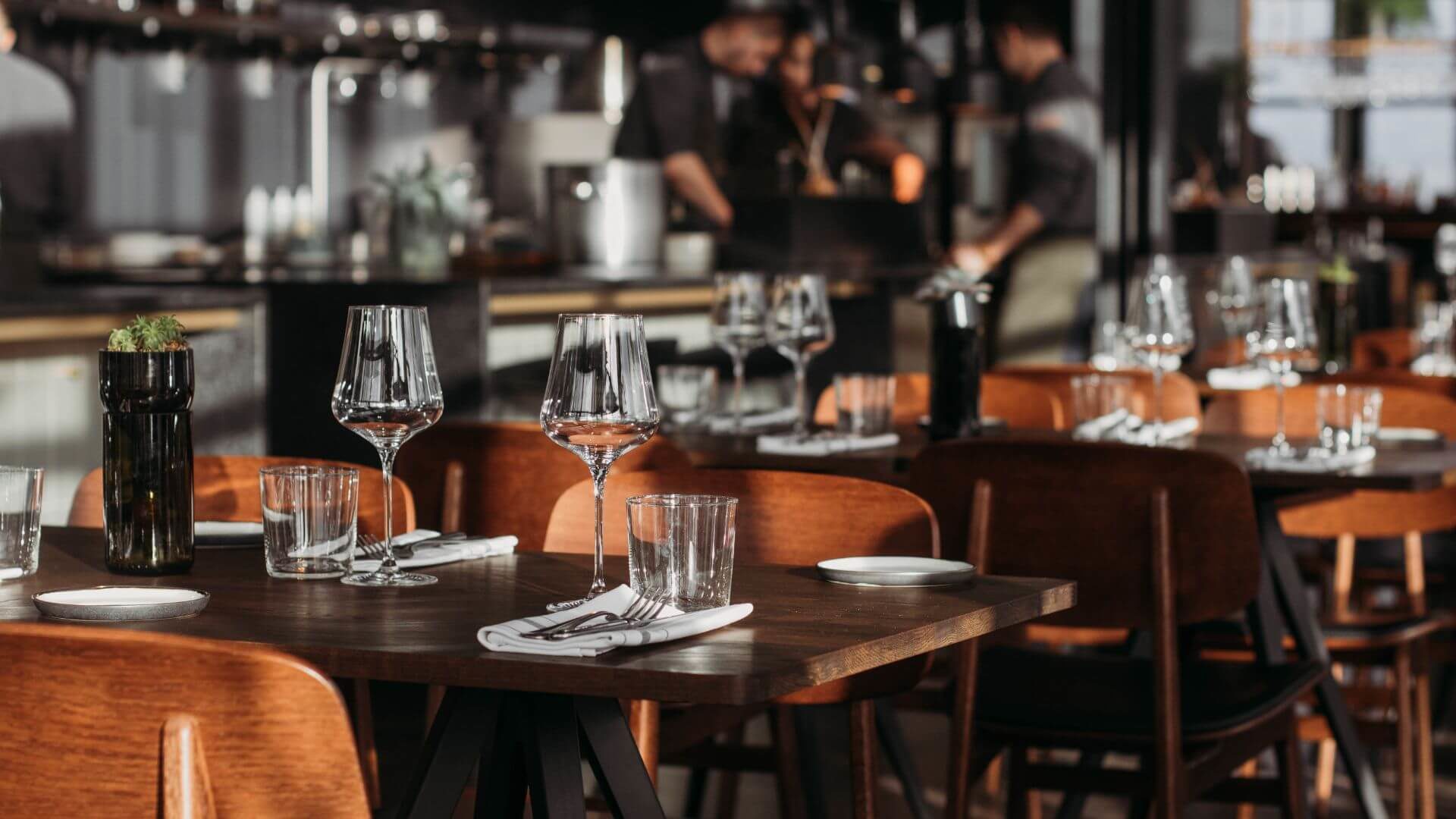 Dining establishment set with crystal glassware and linen napkins, plant in ceramic container.