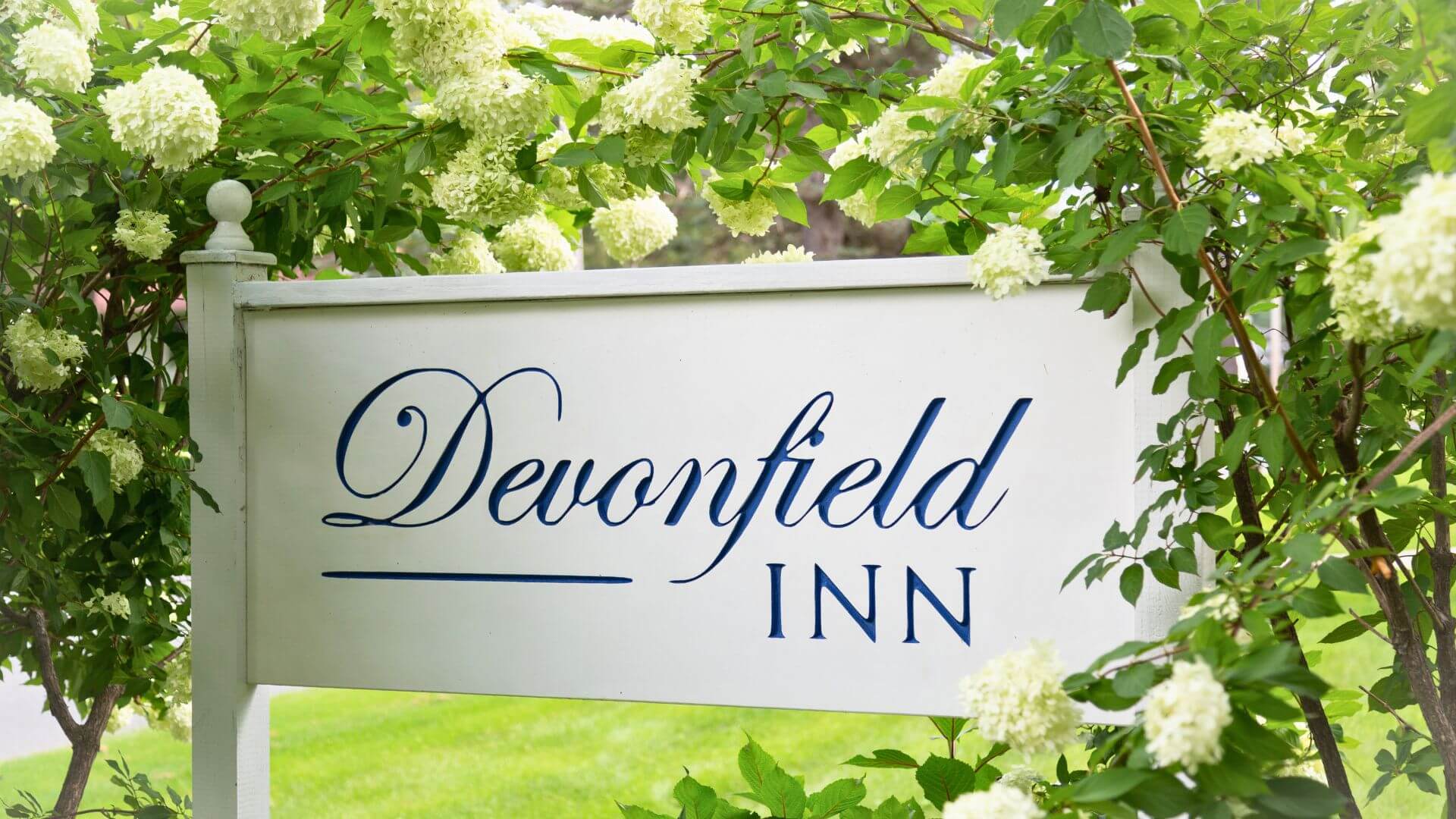 The Devonfield Inn sign surrounded by white flowering plants and greenery.