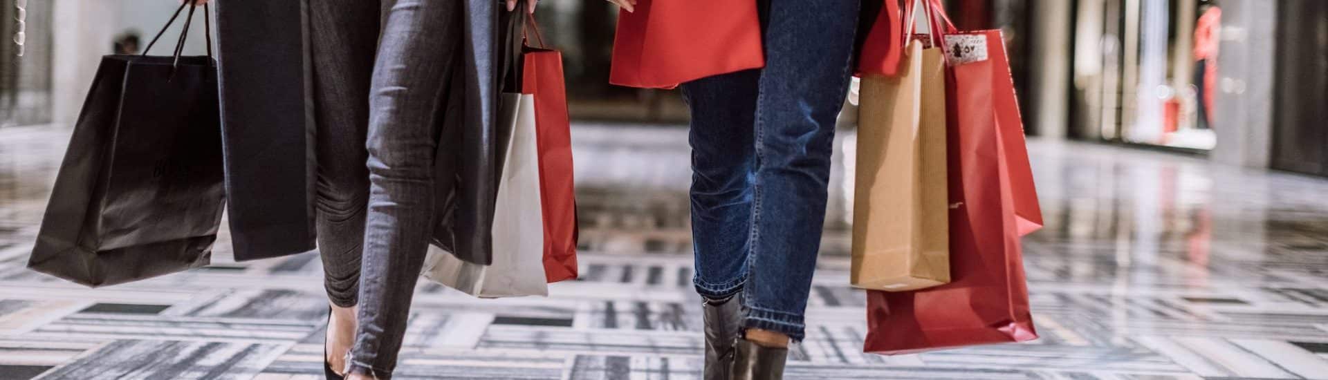 View of two people waist down holding shopping bags and walking through a mall.