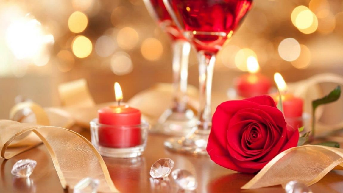 Sparkling light background with candles, a red rose, twirling ribbon and two glasses of wine