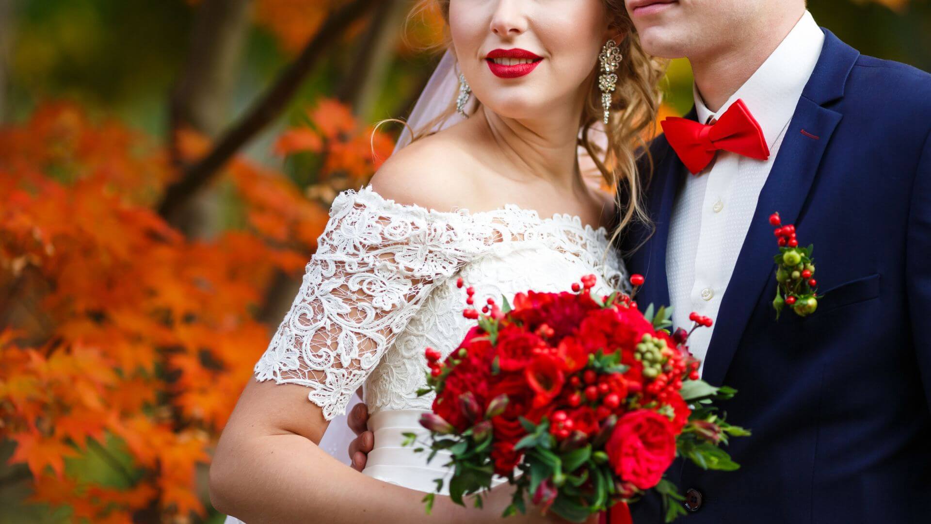 Bridal couple in each other’s arms against a backdrop of red fall foliage