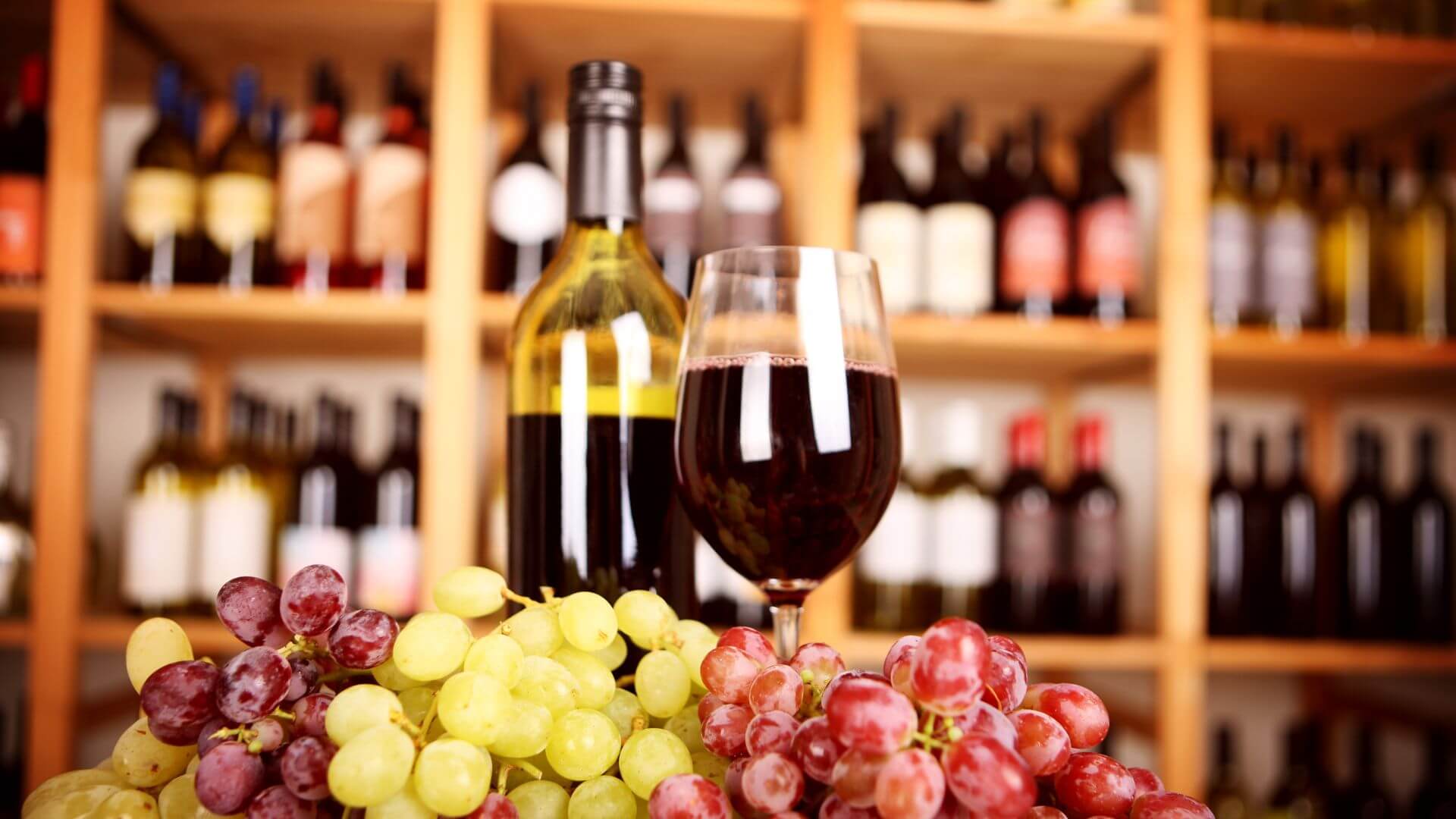 Background of wine on shelves with bottle and goblet of wine and grape bunches in foreground
