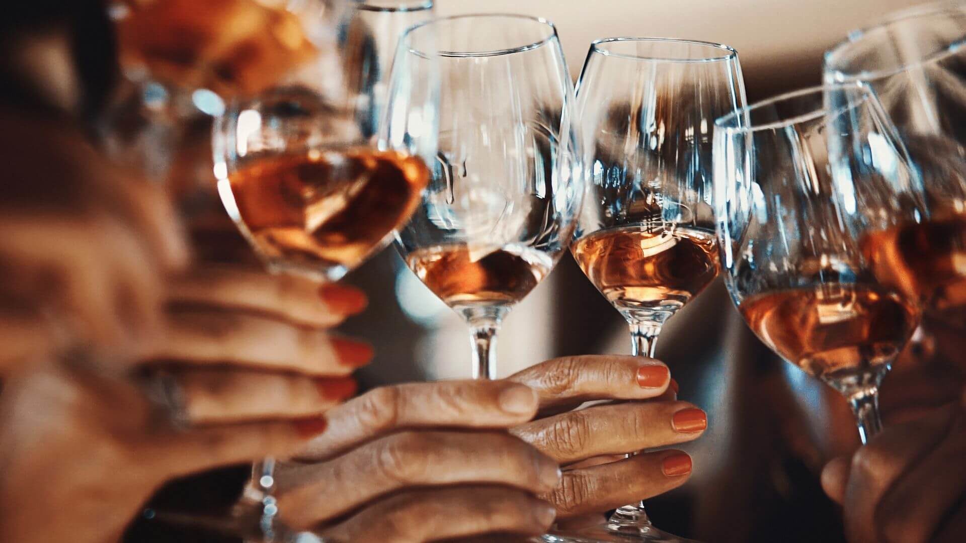 Hands holding clear wine glasses with red wine clinking together.