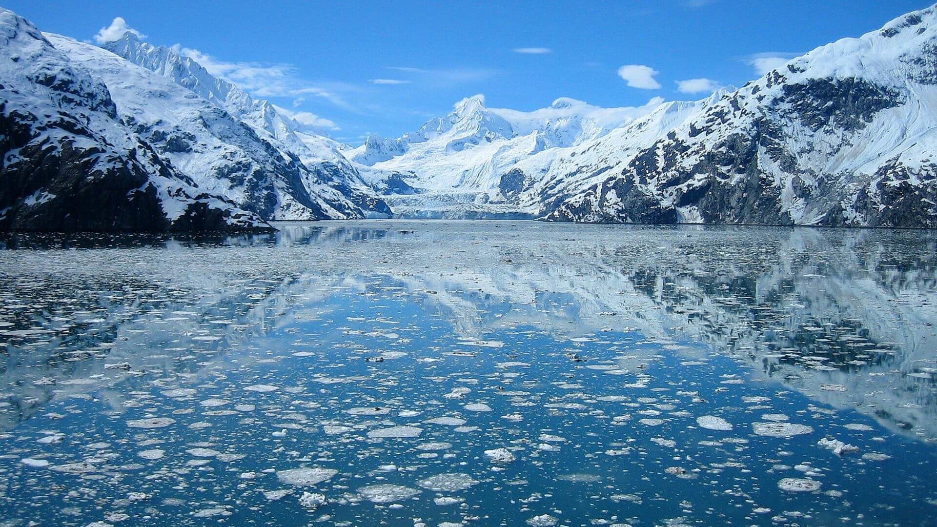 Snow-capped mountains reflecting in ice covered lake.