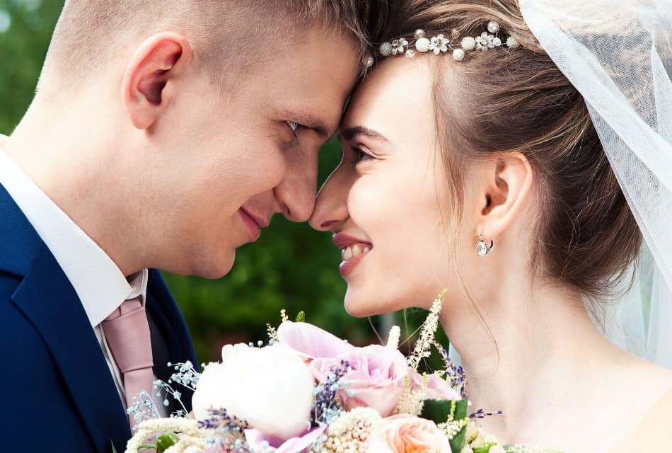 Man in blue suit and woman in white dress touching foreheads and smiling at each other