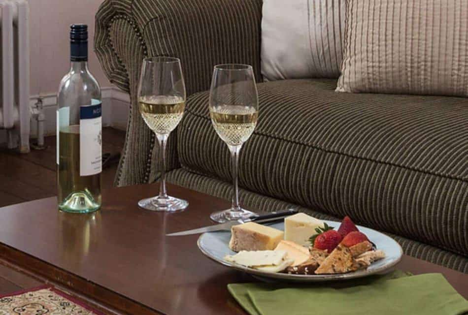 Bottle of wine, two glasses of wine, and plate with cheese and fruit on wooden coffee table