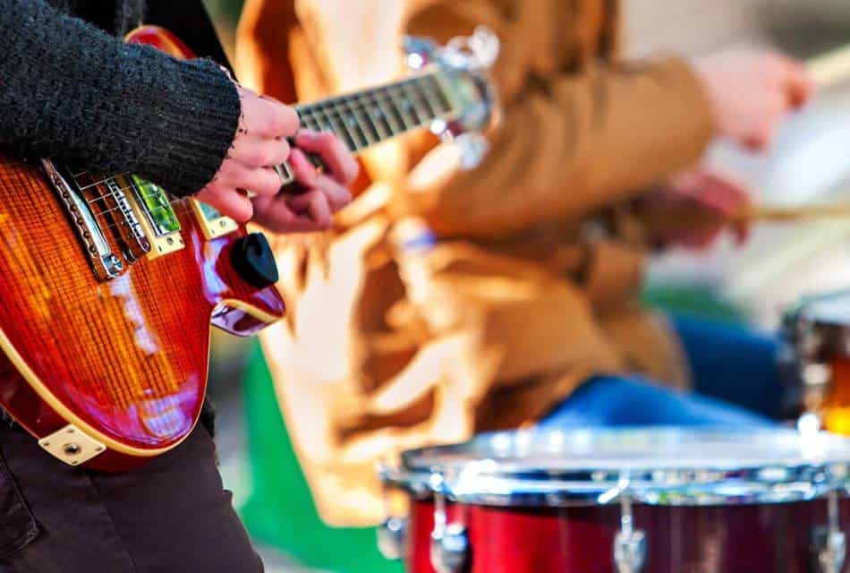 Close up view of a person playing a guitar and a person playing the drums