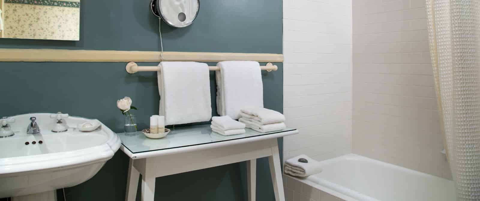 Bathroom with dark teal walls, white sink, white table, and white tub with shower