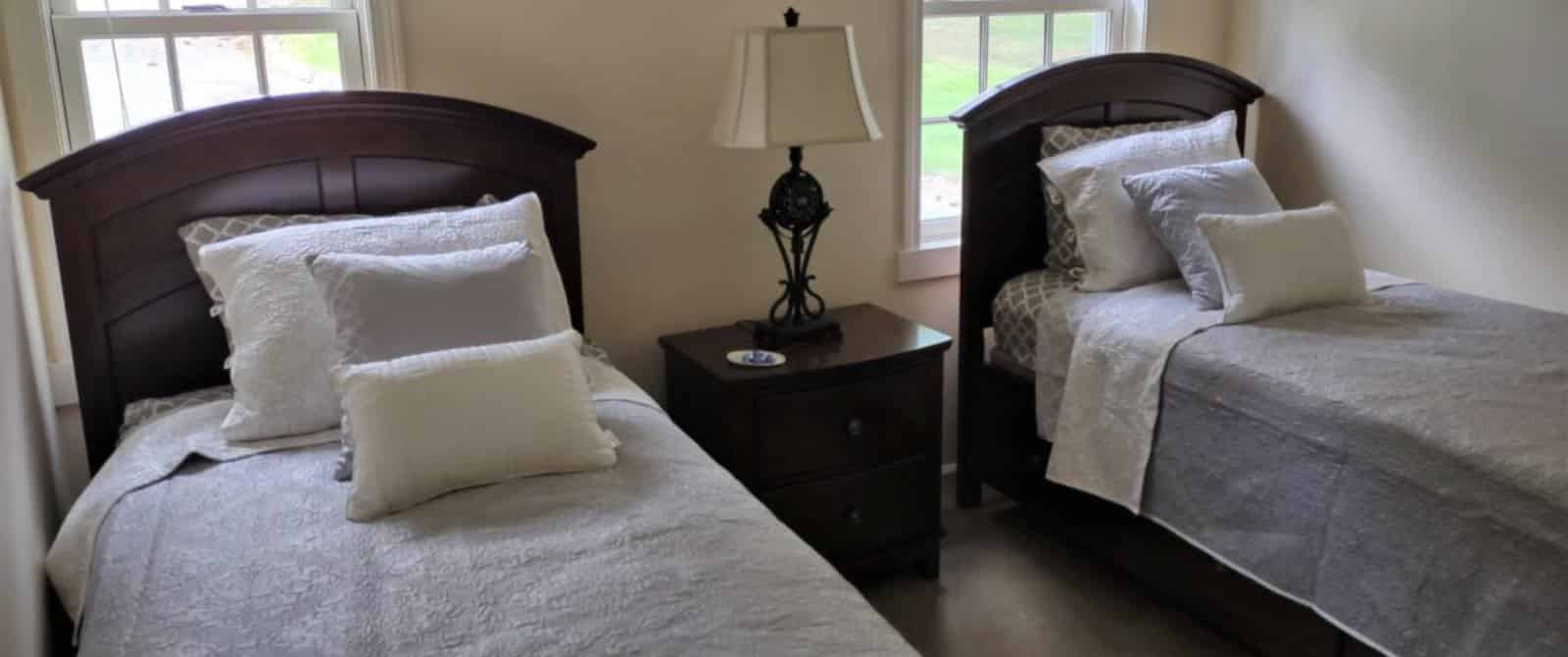 Bedroom with light colored walls, white trim, hardwood flooring, twin beds, gray bedding, and wooden nightstand