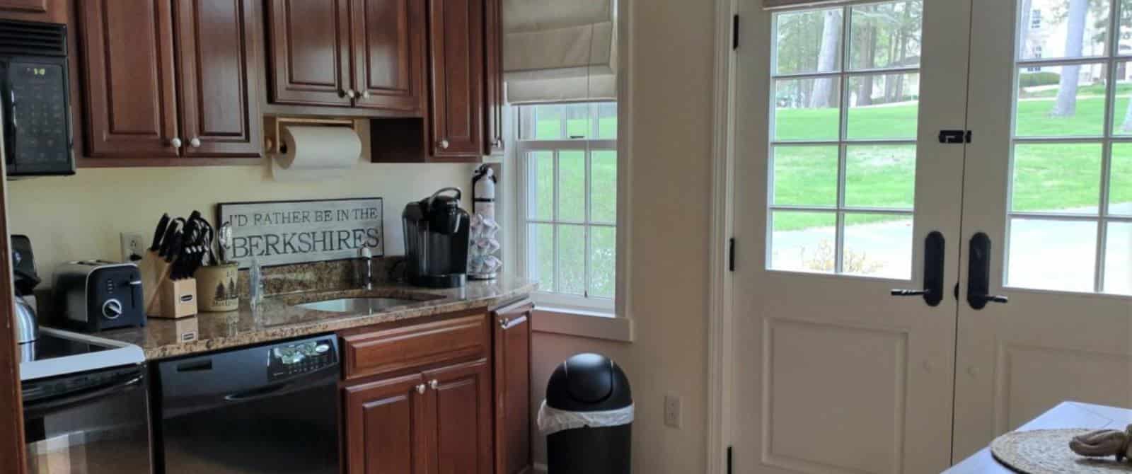 Kitchen with dark wooden cabinets, quartz countertop, black appliances, and double doors to the outside