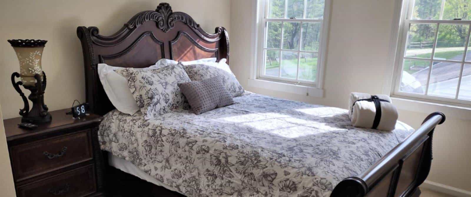 Bedroom with light colored walls and carpetting, dark wooden sleigh bed, floral bedding, wooden dresser, and windows