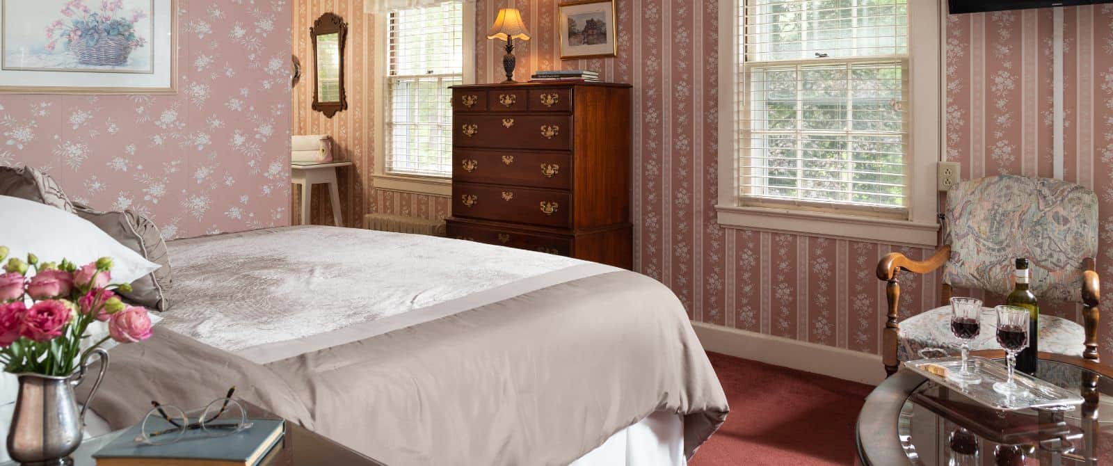 Bedroom with dark floral wallpaper, red carpeting, gray bedding, wooden dresser, and upholstered wooden chair