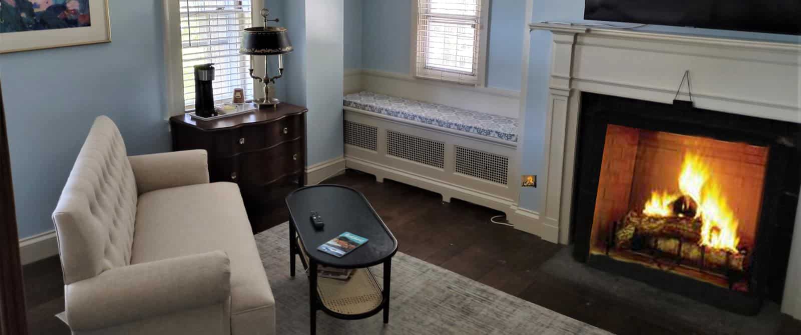 Bedroom sitting area with upholstered loveseat, wooden coffee table, wooden dresser, and fireplace