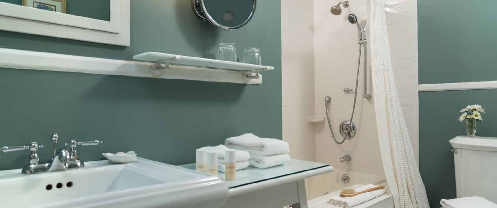 Bathroom with dark teal walls, white sink, white table, and white tub with shower