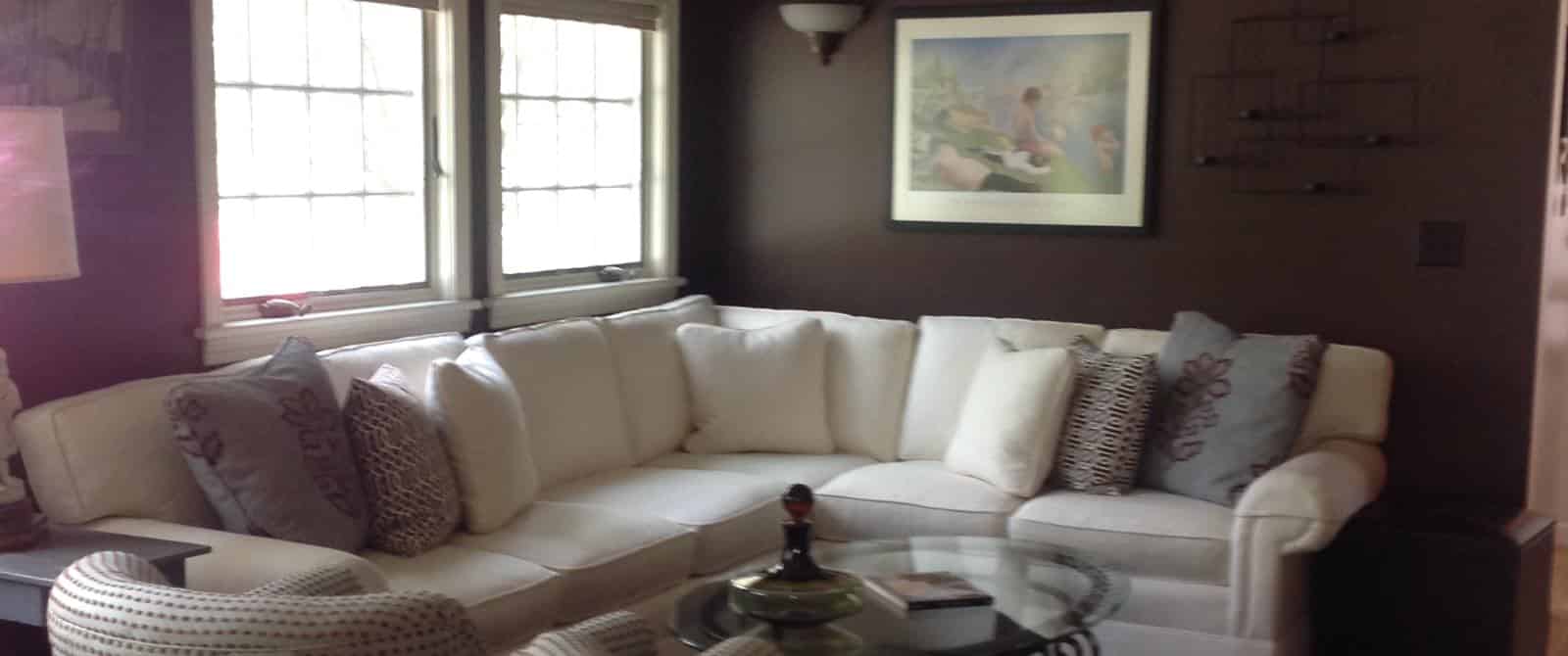 Gathering area with dark walls, hardwood flooring, large white sectional, glass coffee table, and two upholstered chairs