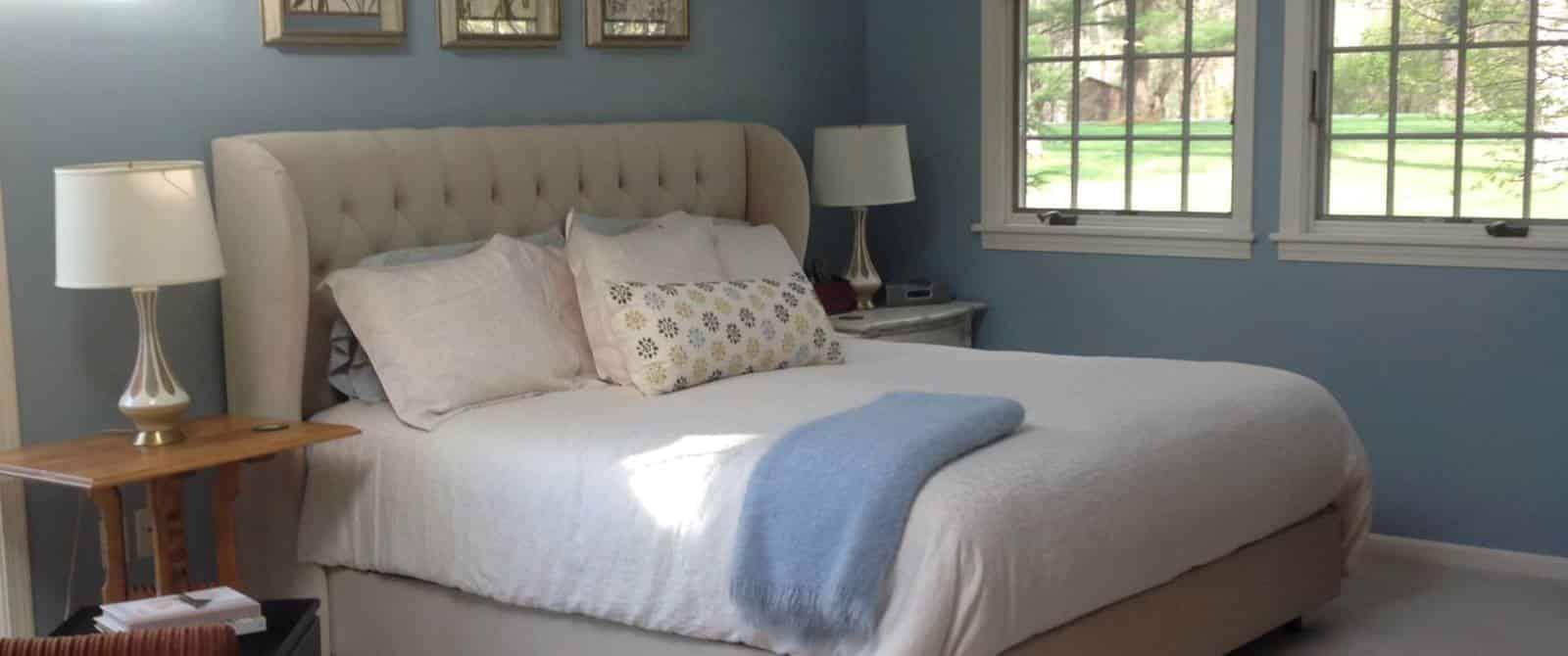 Bedroom with blue walls, white trim, upholstered headboard, white bedding, and multiple windows