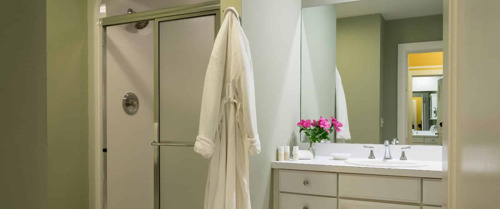 Bathroom with light green walls, white sink, vanity with drawers, and stand-up shower