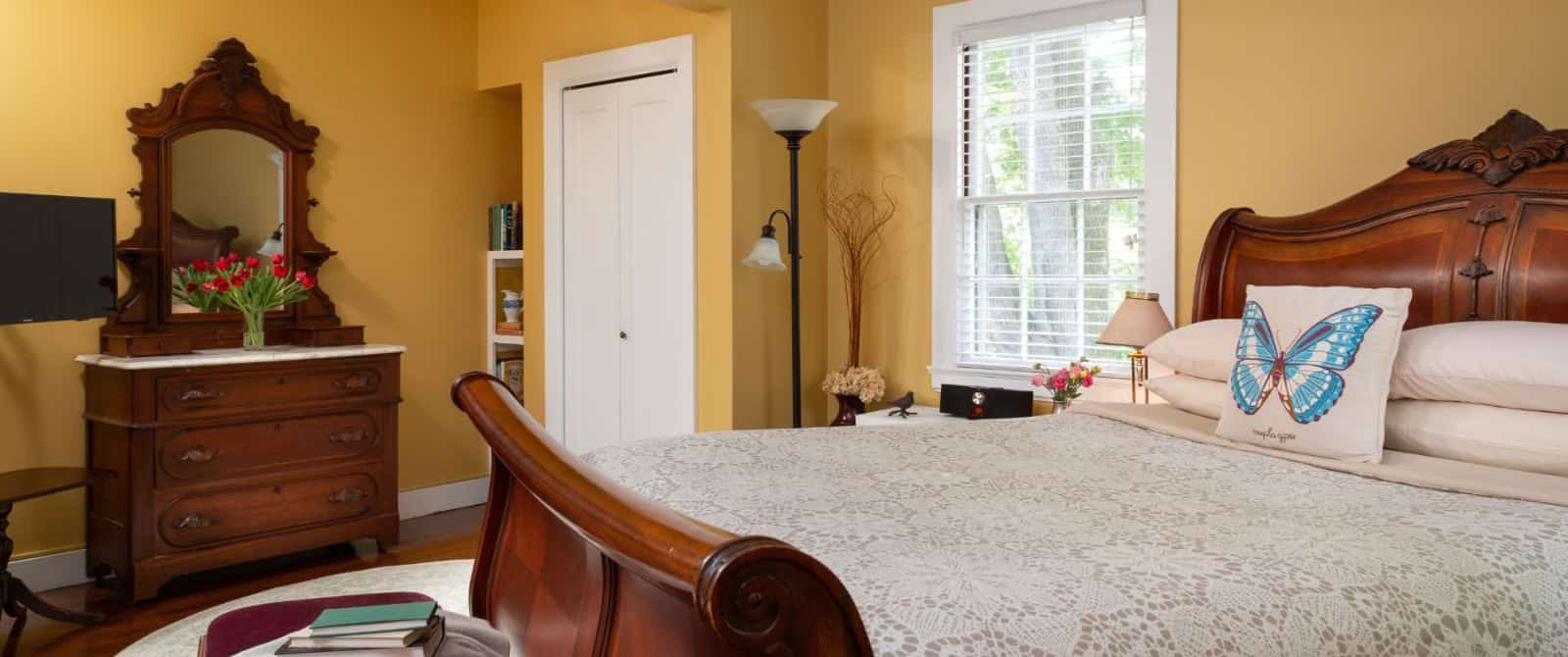 Bedroom with yellow walls, white trim, hardwood flooring, wooden sleigh bed, wooden dresser, and window