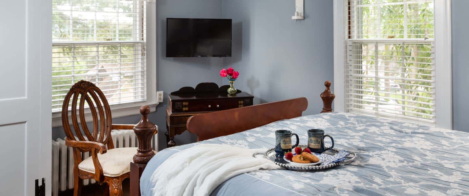 Bedroom with blue walls, white trim, blue bedding, wall-mounted flat-screen TV, and antique wooden chair
