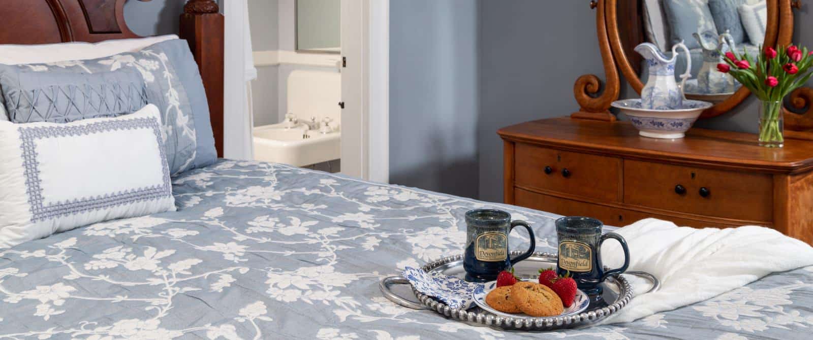 Bedroom with blue walls, wooden bed, blue bedding, and view into bathroom