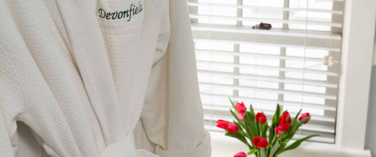 Close up view of white robe with Devonfield embroidery and bouquet of red tulips