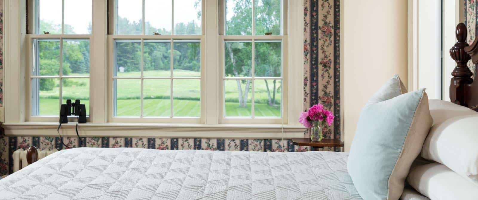 Bedroom with floral and striped wallpaper, hardwood flooring, wooden bed, light blue bedding, and large window