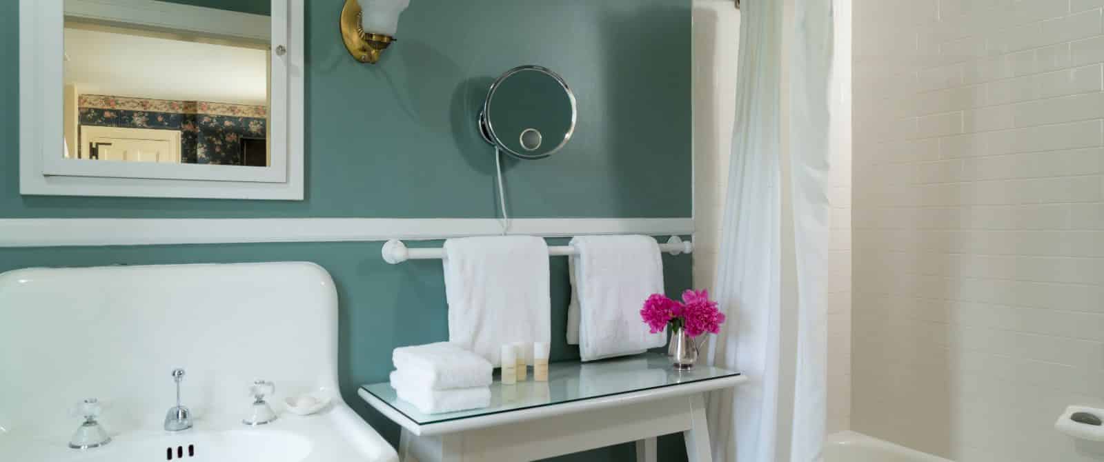 Bathroom with dark teal walls, white sink, white table, and white tub with shower