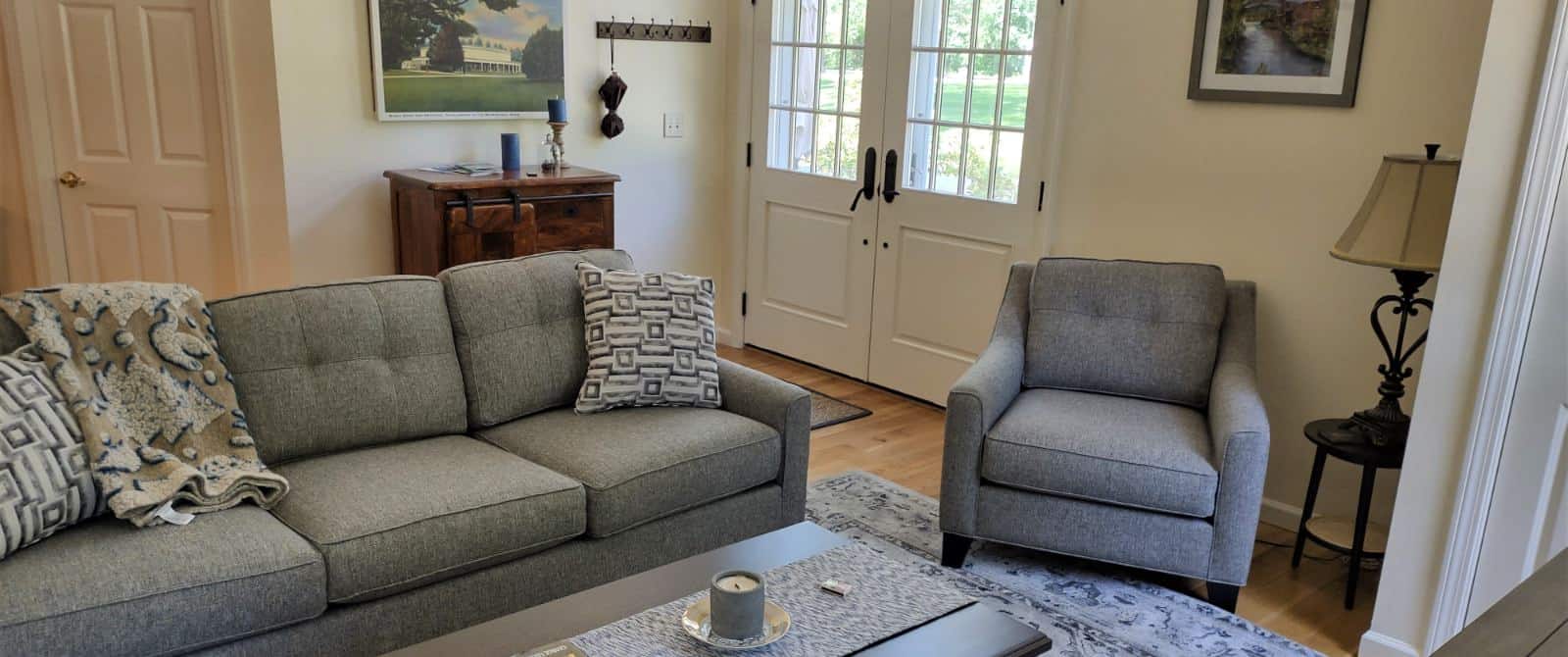 Gathering room with light colored walls, hardwood flooring, upholstered coach and chair and wooden coffee table