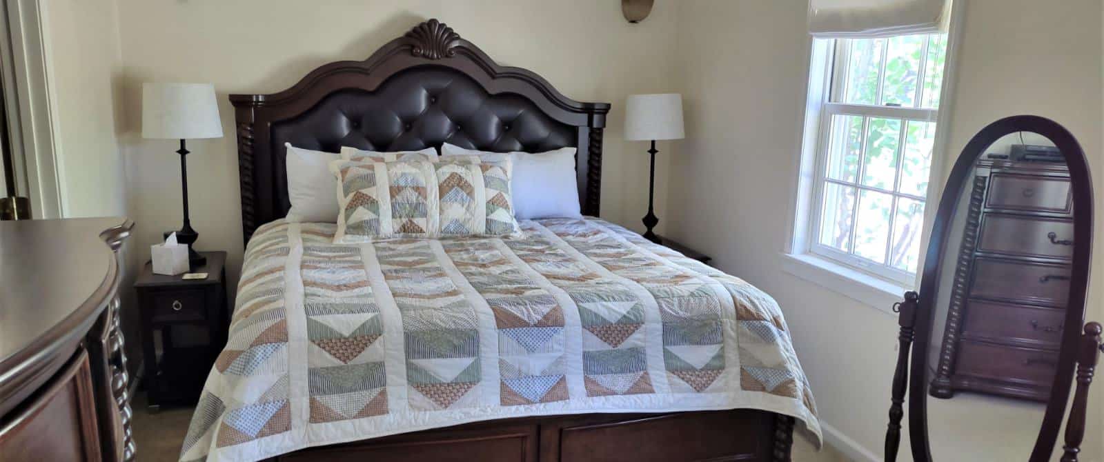 Bedroom with white walls, dark wood and leather upholstered headboard, multicolored bedding, two nightstands, and two lamps