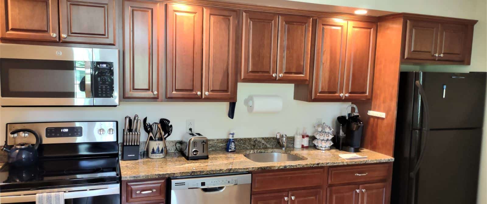 Kitchen with dark wooden cabinets, black and stainless steel appliances, and quartz countertop