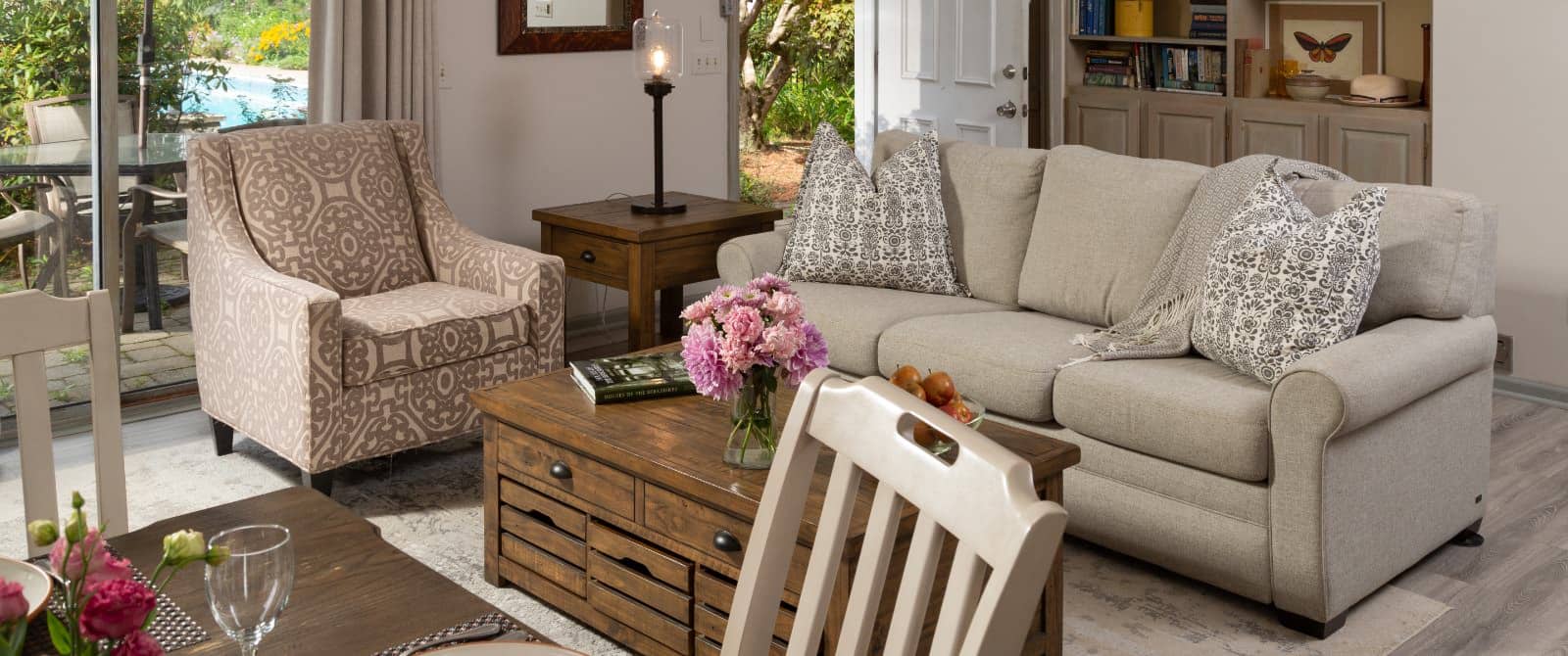 Large gathering area with light colored walls, hardwood flooring, upholstered sofa and chair, wooden coffee table, and dining area