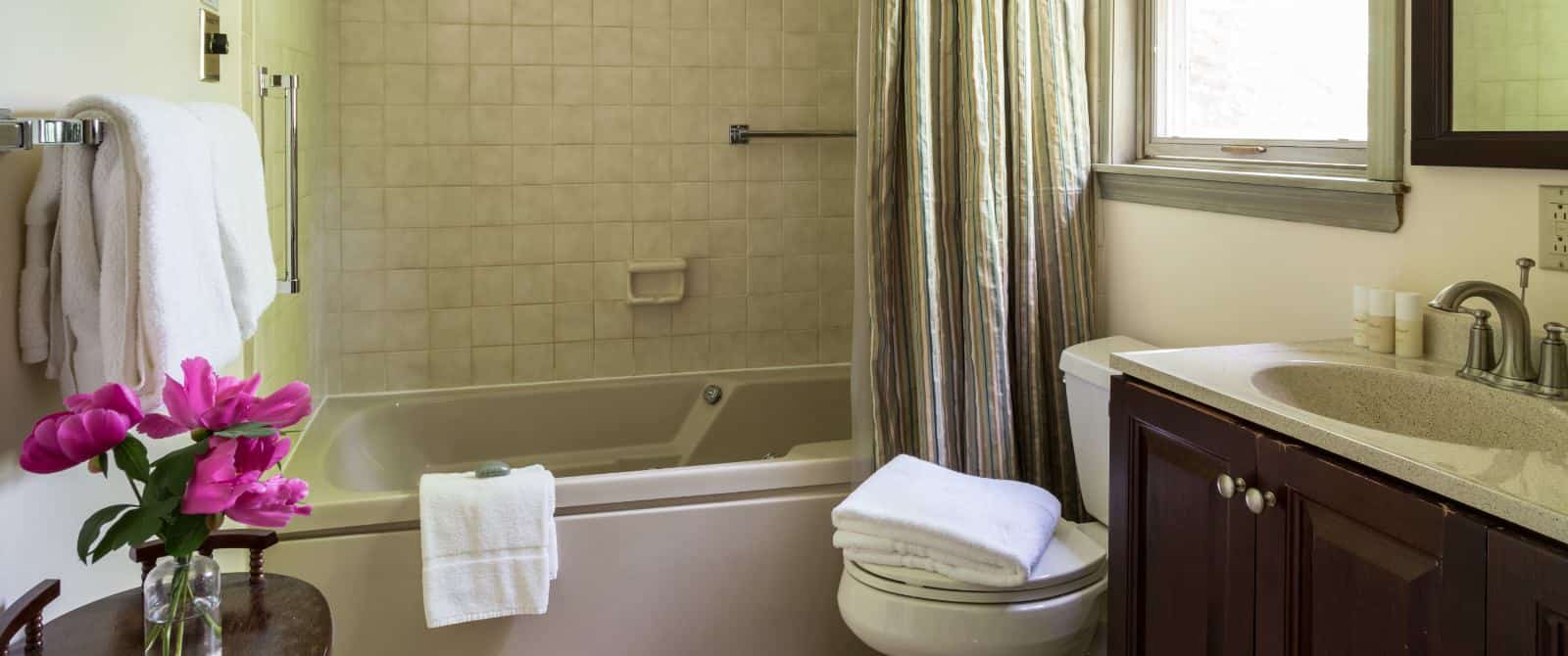 Batrhoom with light colored walls, dark wooden vanity, quartz top, wooden mirror, and tub with shower