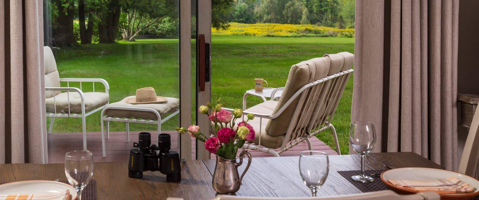 Dining area with wooden table and open glass sliding door out to a deck with patio furniture and view or green grass and trees in the background