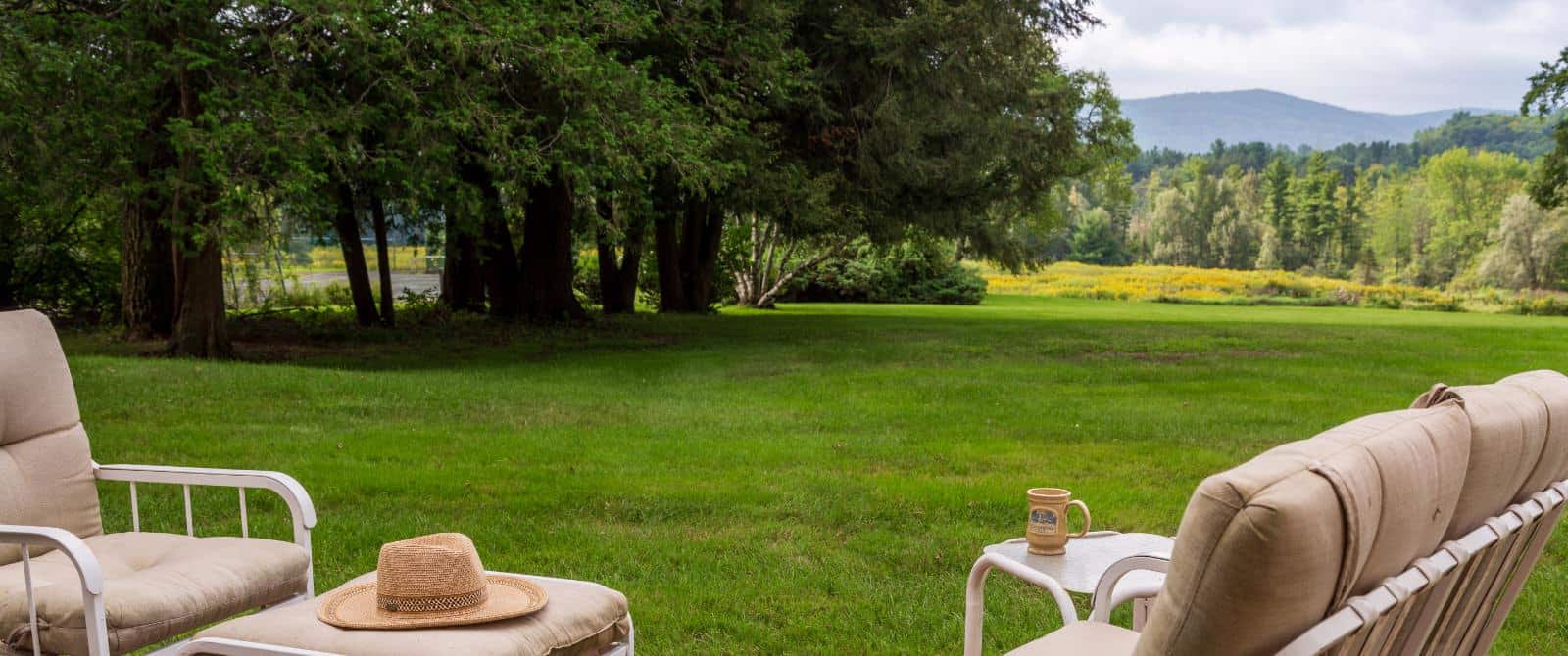 Patio furniture on deck with view of large green grassy area and large trees in the background