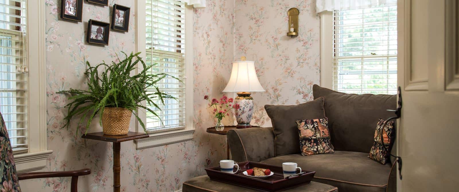 Bedroom sitting area with floral wallpaper, dark brown upholstered oversized chair and ottoman, and multiple windows