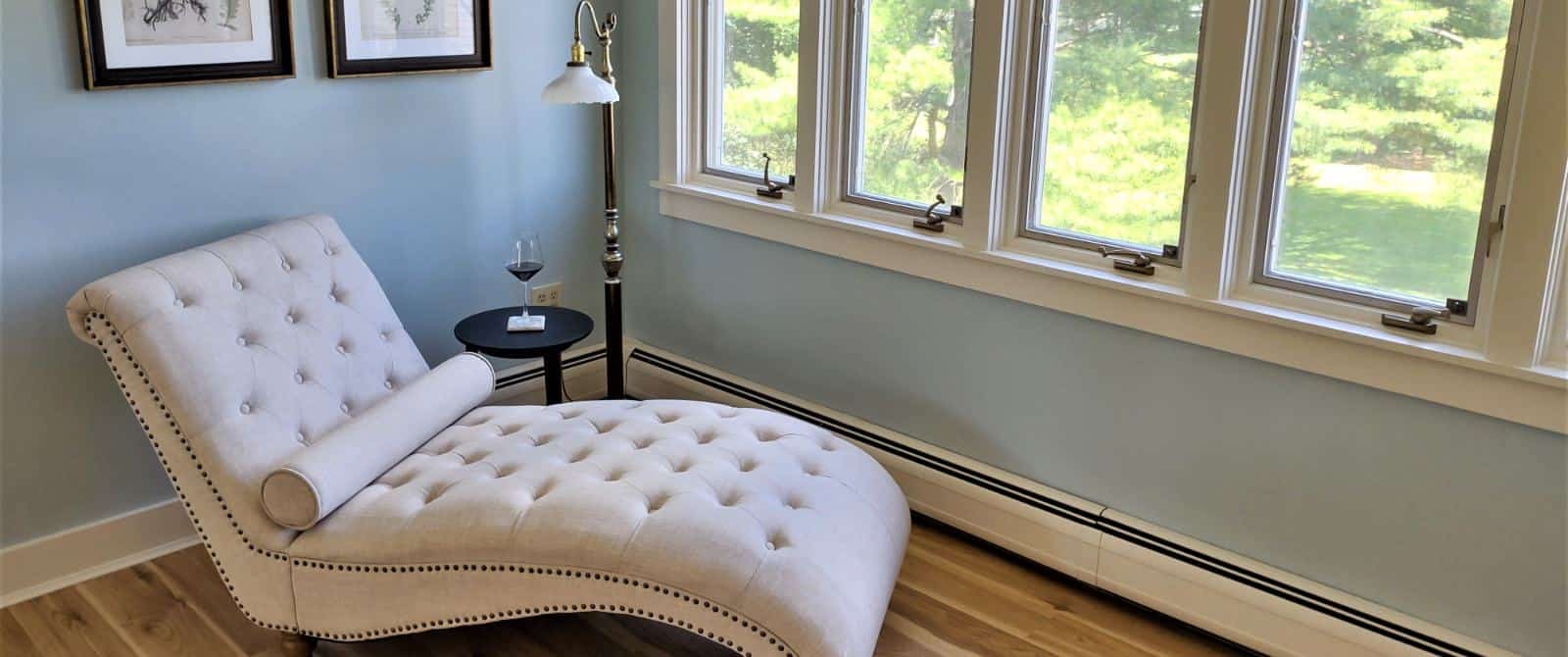 Bedroom with light blue walls, white trim, hardwood flooring, and upholstered chaise