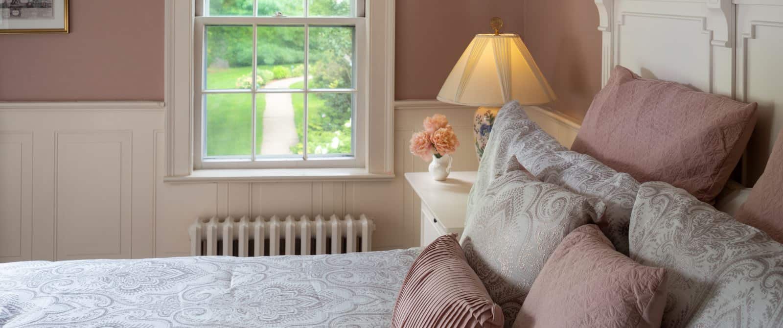 Bedroom with peach walls, white trim, light paisley bedding, white nightstand, and window